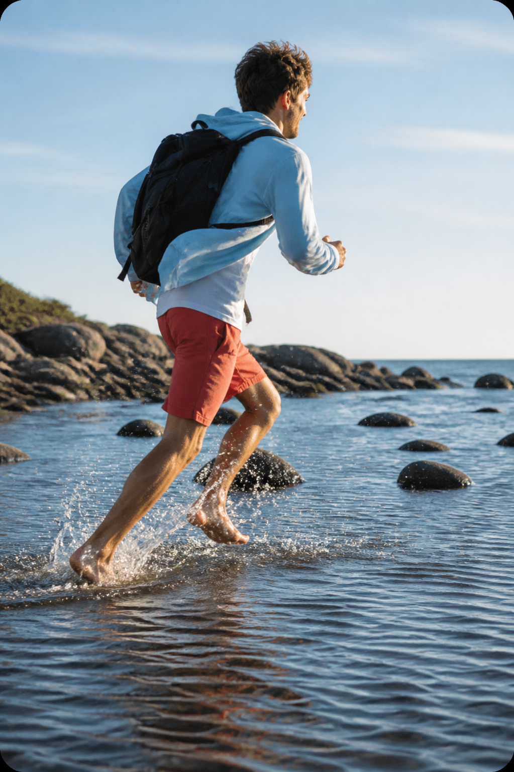 A man with a backpack running through shallow coastal water